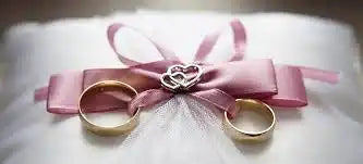 Two gold wedding rings tied with a pink ribbon bow.